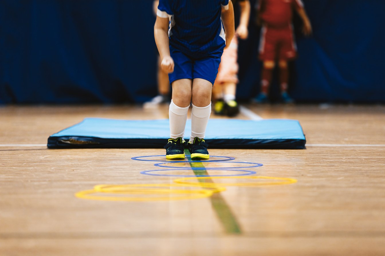 Group of Children in School Age Jumping over Obstacles at Indoor